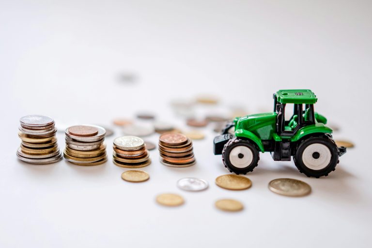 A miniature green tractor beside stacks of coins in a creative still life scene.